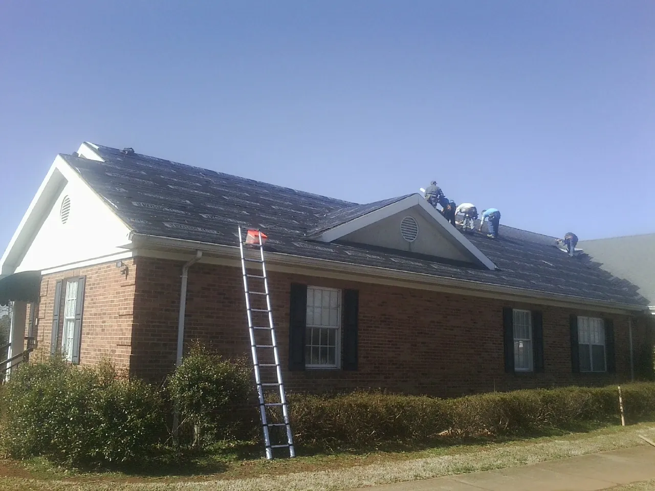 Crew tearing shingles off a brick ranch roof with a ladder set — Emergency Roof Repair work by our crew in Enfield