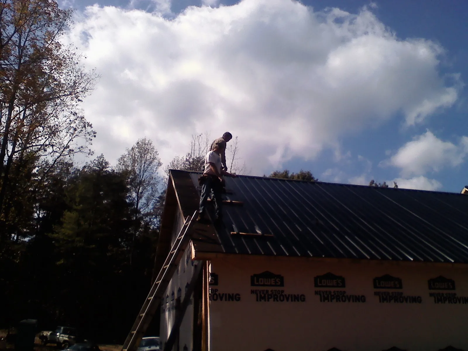 Roofer fastening dark metal panels high against a cloudy sky, from a Roof Inspection job in Enfield