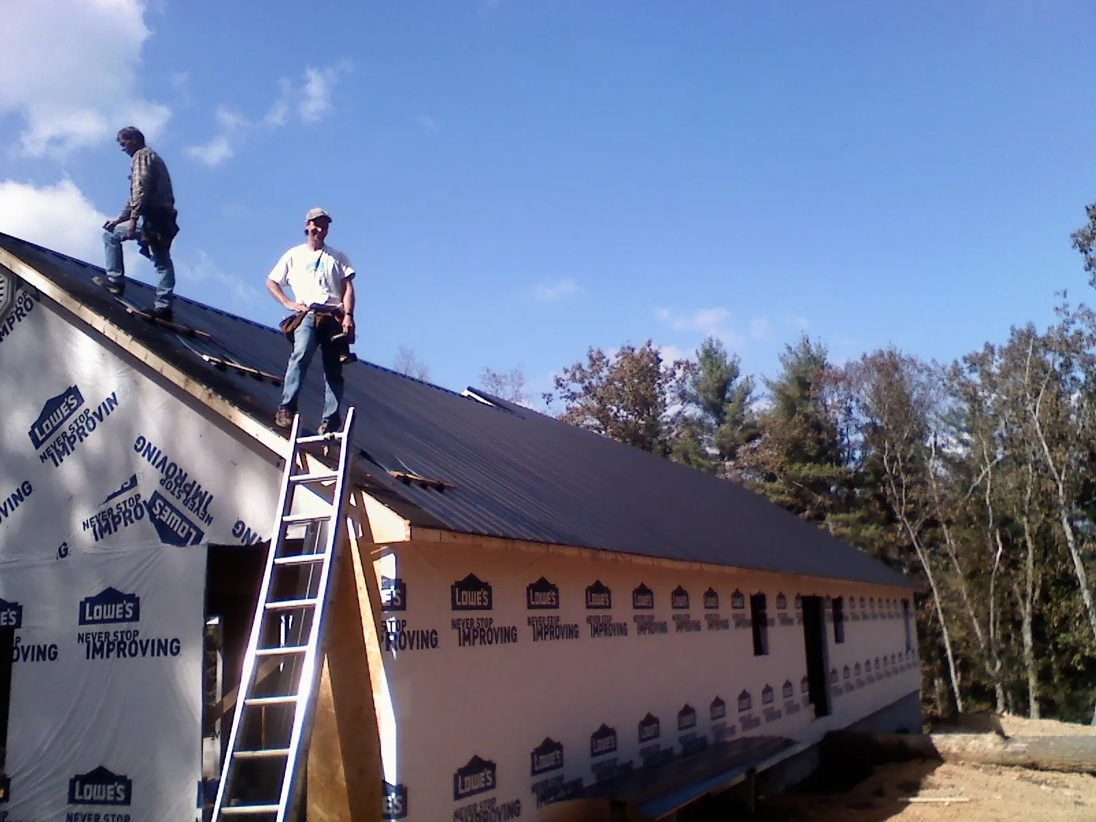 Two roofers standing on a long dark metal roof over a wrapped building in Enfield
