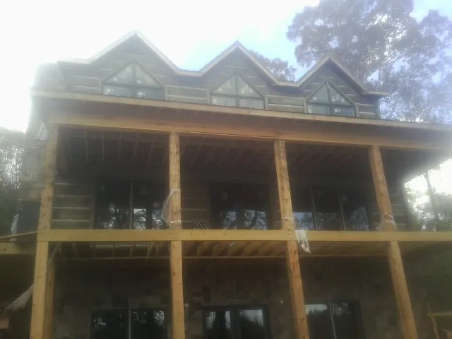 Dormers and porch framing on a large log home under construction — Roof Coating work by our crew in Enfield