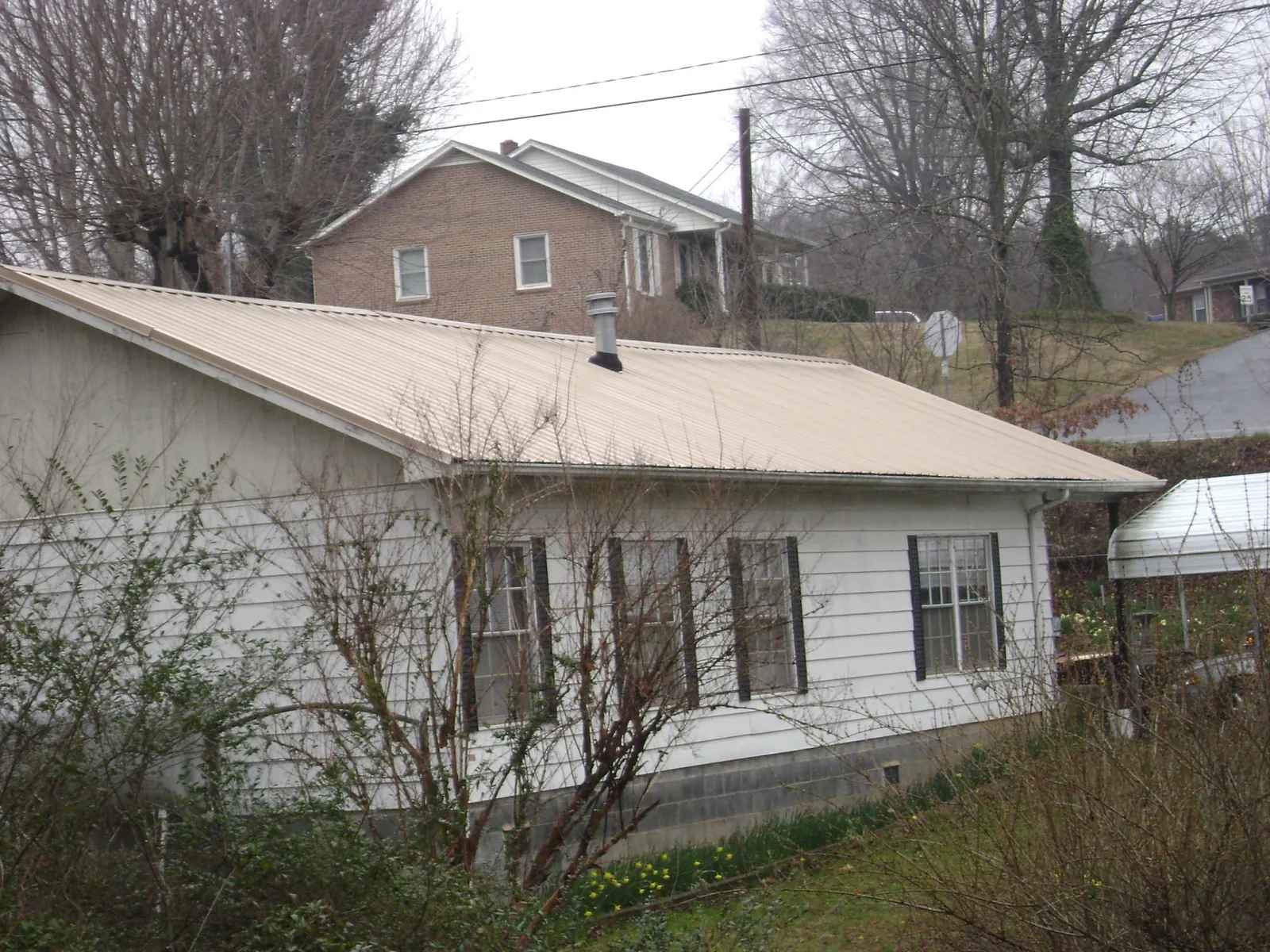 Tan metal roof on a white sided house set into a hillside — Commercial Roofing by Roofing Brothers in Enfield